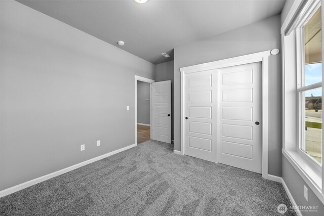 unfurnished bedroom featuring carpet floors, baseboards, multiple windows, and a closet