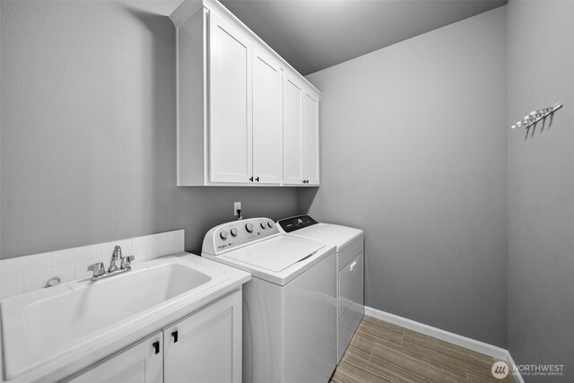 clothes washing area with cabinet space, a sink, light wood finished floors, separate washer and dryer, and baseboards