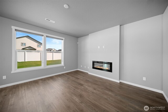 unfurnished living room with baseboards, a glass covered fireplace, visible vents, and dark wood-style floors