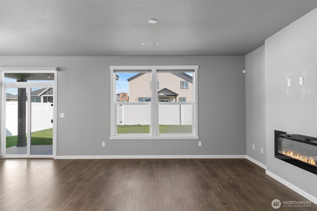 unfurnished living room featuring baseboards, a textured ceiling, dark wood finished floors, and a glass covered fireplace