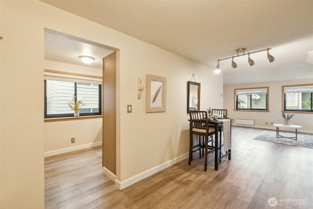 hallway featuring baseboards, wood finished floors, and rail lighting