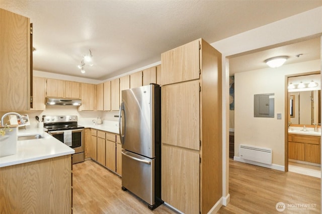 kitchen featuring baseboard heating, a sink, under cabinet range hood, light brown cabinets, and stainless steel appliances