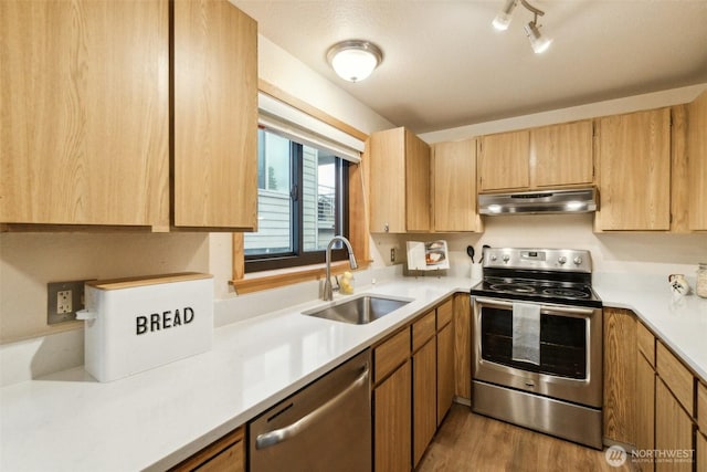 kitchen with wood finished floors, a sink, light countertops, under cabinet range hood, and stainless steel appliances