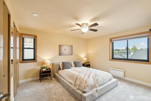 bedroom featuring multiple windows, a baseboard heating unit, and light colored carpet