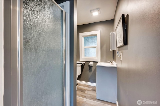 bathroom featuring wood finished floors, a shower stall, vanity, baseboards, and toilet