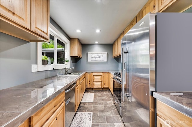 kitchen featuring appliances with stainless steel finishes, light brown cabinetry, a sink, stone finish floors, and recessed lighting
