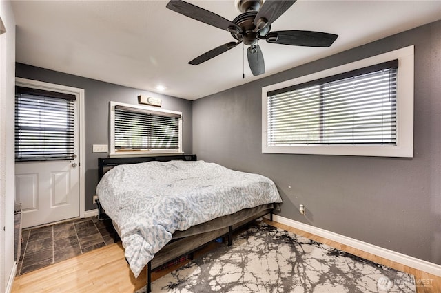 bedroom featuring multiple windows, baseboards, ceiling fan, and wood finished floors