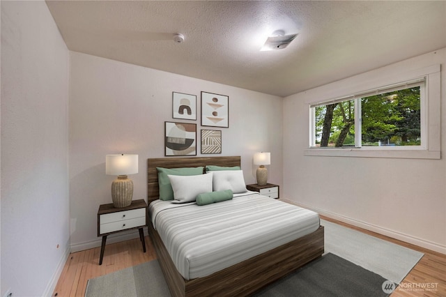 bedroom featuring wood finished floors, a textured ceiling, and baseboards