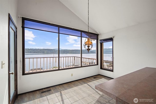 unfurnished dining area with a water view, high vaulted ceiling, wood finished floors, and visible vents