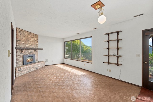 unfurnished living room with baseboards, a brick fireplace, a textured ceiling, and visible vents