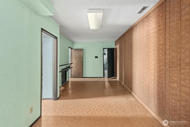 corridor with baseboards, visible vents, a textured wall, and light floors