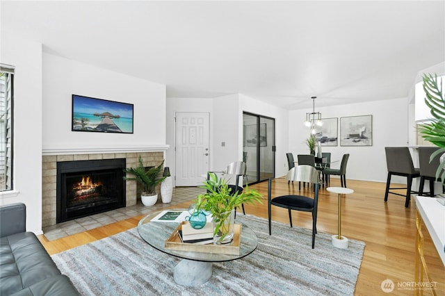 living room with a notable chandelier, a tiled fireplace, and wood finished floors