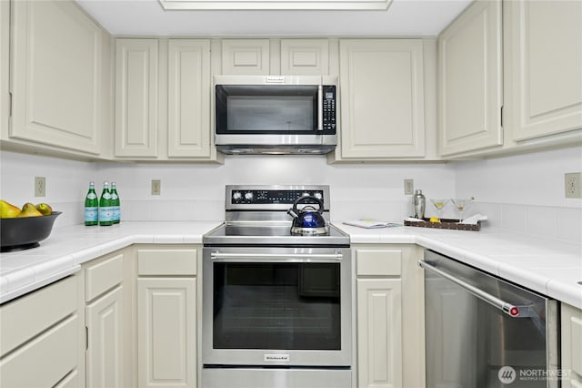 kitchen featuring tile counters, appliances with stainless steel finishes, and white cabinets