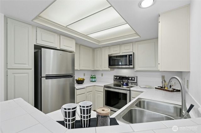 kitchen with tile countertops, appliances with stainless steel finishes, a sink, and a raised ceiling