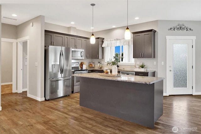 kitchen featuring pendant lighting, dark wood-style floors, a center island, light stone counters, and appliances with stainless steel finishes