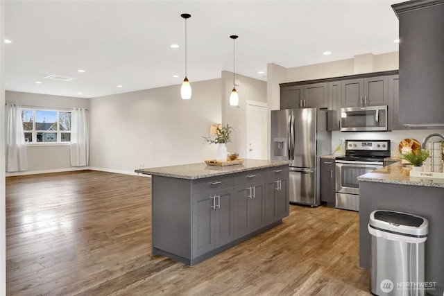 kitchen with hanging light fixtures, appliances with stainless steel finishes, light stone counters, light wood-style floors, and a center island