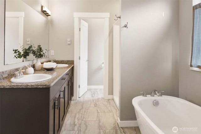 bathroom with double vanity, a freestanding bath, a sink, and marble finish floor