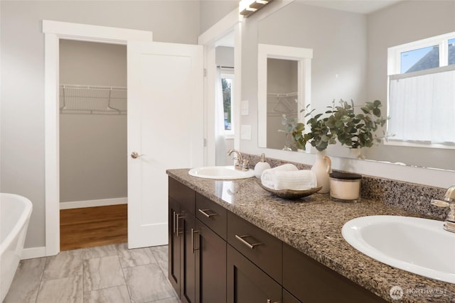 bathroom with double vanity, a sink, a freestanding bath, and a spacious closet
