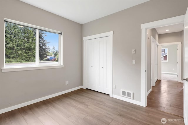 unfurnished bedroom featuring baseboards, a closet, wood finished floors, and visible vents