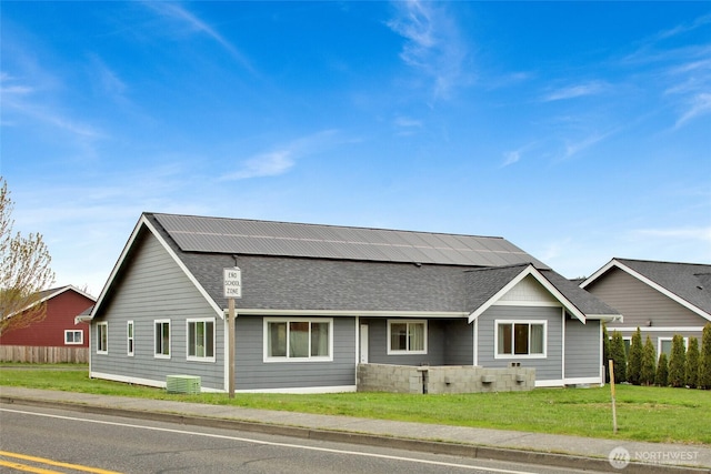 view of front of property featuring a front yard, cooling unit, roof mounted solar panels, and roof with shingles