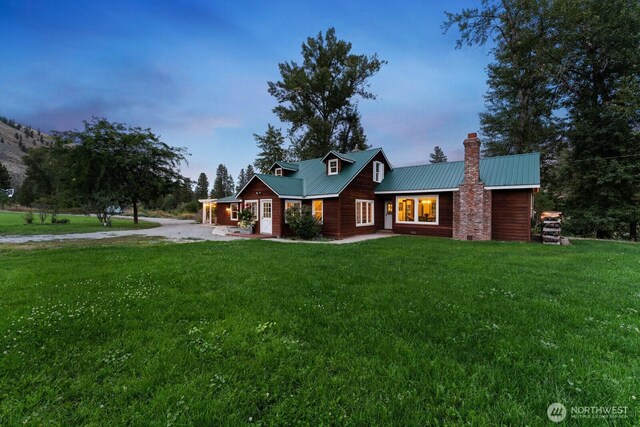 view of front of home with a chimney, driveway, a front yard, and metal roof