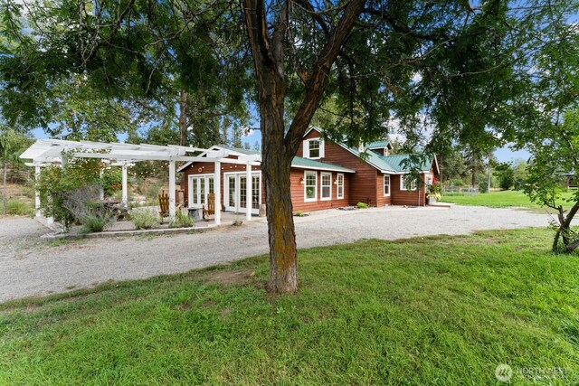view of front facade with a pergola, a front yard, french doors, driveway, and metal roof