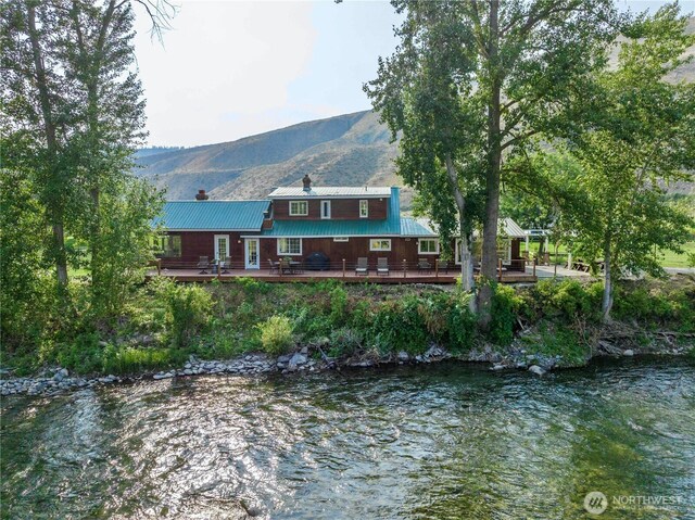 rear view of property featuring a deck with water view, a chimney, and metal roof