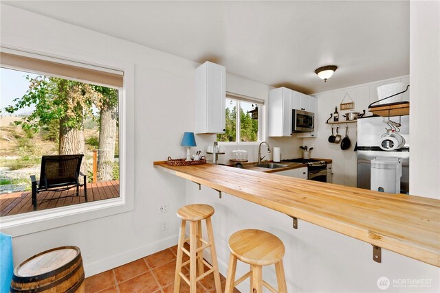 kitchen with white cabinets, butcher block countertops, stainless steel appliances, light tile patterned floors, and a kitchen bar