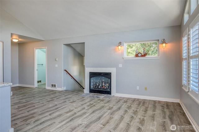 659 Chinook Ave SE, Ocean Shores, WA 98569 - unfurnished living room with wood finished floors, a tiled fireplace, vaulted ceiling, plenty of natural light, and baseboards