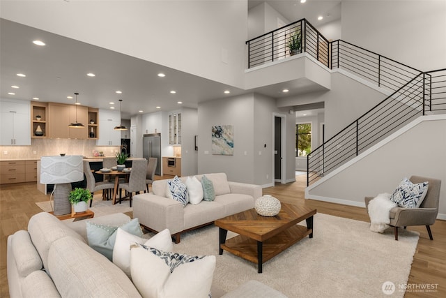 living room featuring stairs, light wood-style floors, recessed lighting, and a high ceiling