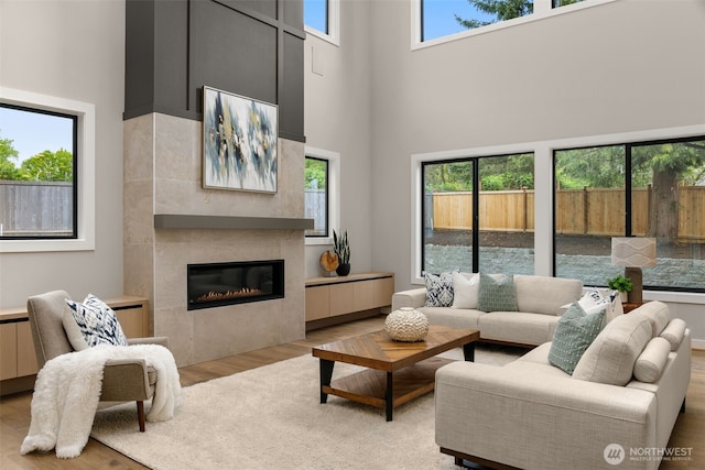 living area featuring a tile fireplace, a wealth of natural light, wood finished floors, and a high ceiling