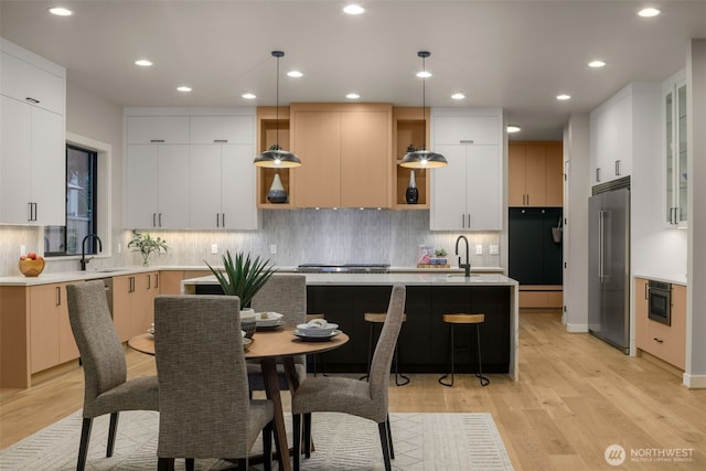 kitchen featuring a sink, open shelves, a kitchen island with sink, light wood finished floors, and appliances with stainless steel finishes