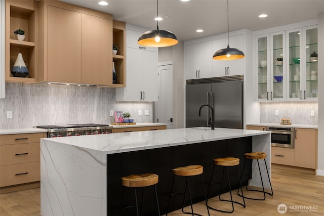 kitchen featuring an island with sink, light wood-type flooring, open shelves, and appliances with stainless steel finishes