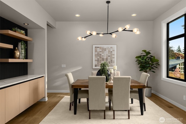dining area featuring light wood-type flooring, a notable chandelier, visible vents, and baseboards