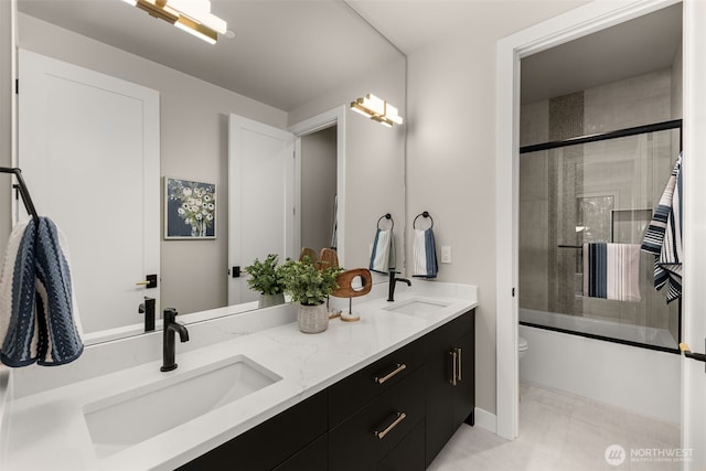 bathroom featuring bath / shower combo with glass door, toilet, double vanity, and a sink