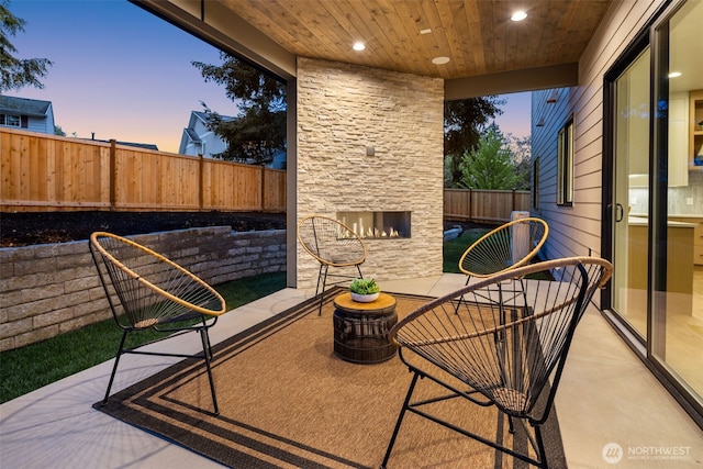 patio terrace at dusk featuring an outdoor stone fireplace and a fenced backyard