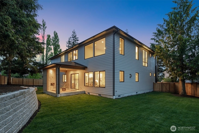 back of property at dusk featuring a yard, a fenced backyard, and crawl space