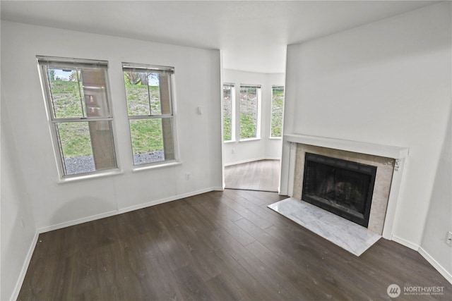 unfurnished living room featuring a high end fireplace, baseboards, plenty of natural light, and wood finished floors
