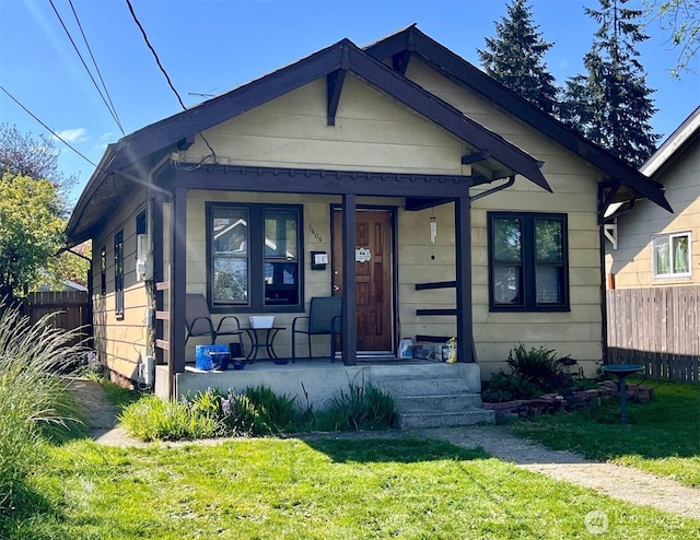bungalow-style home with covered porch, fence, and a front lawn