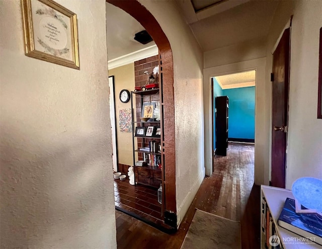 hall featuring arched walkways, a textured wall, baseboards, and wood finished floors