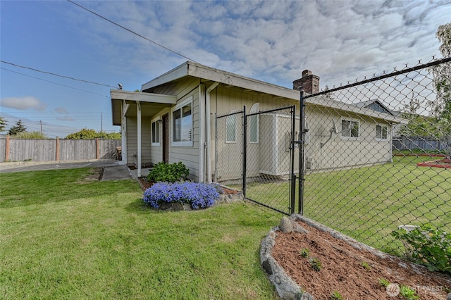view of side of home with a yard, fence, a chimney, and a gate