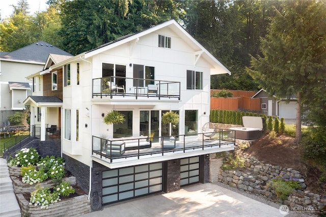 back of house featuring a balcony, an attached garage, fence, and concrete driveway