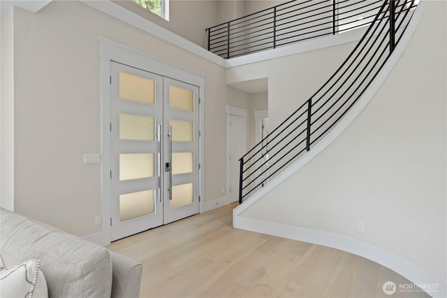 foyer featuring wood finished floors, stairs, a towering ceiling, baseboards, and french doors