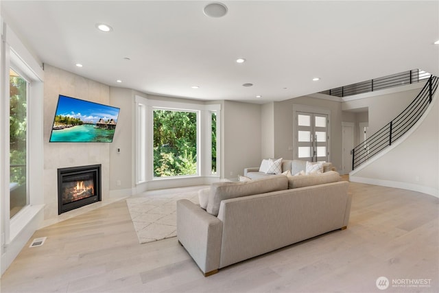 living area with a large fireplace, light wood-type flooring, recessed lighting, stairs, and baseboards
