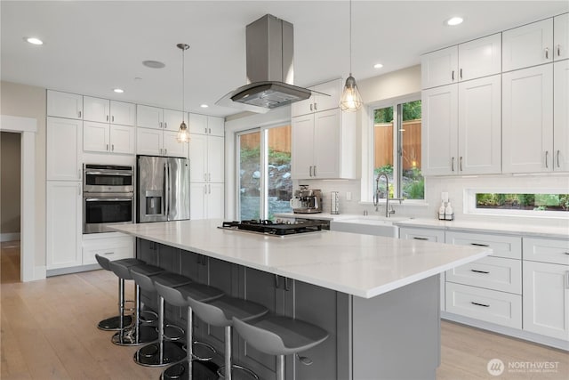 kitchen featuring stainless steel appliances, a sink, island exhaust hood, a kitchen island, and a breakfast bar area