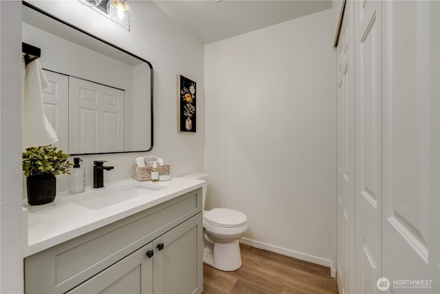 bathroom featuring vanity, baseboards, wood finished floors, and toilet