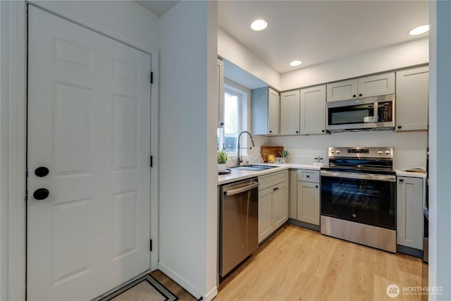 kitchen with light countertops, stainless steel appliances, a sink, and light wood finished floors