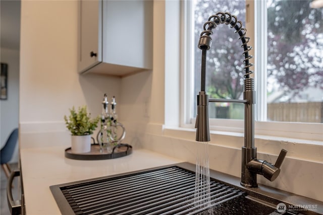 details featuring a sink, light countertops, backsplash, and white cabinetry
