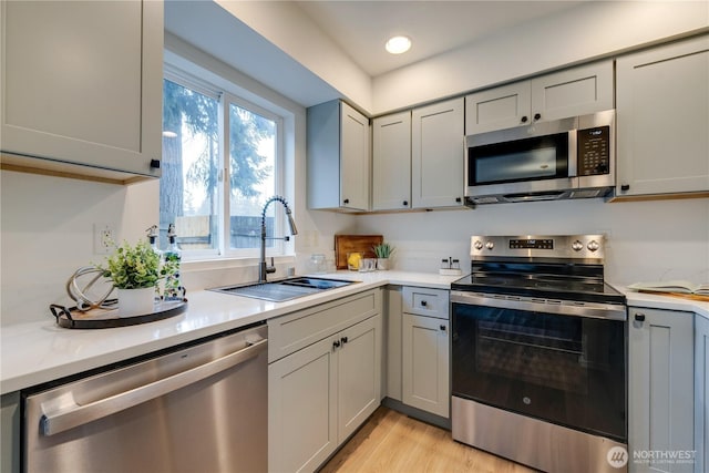 kitchen with light wood-type flooring, light countertops, gray cabinets, a sink, and appliances with stainless steel finishes