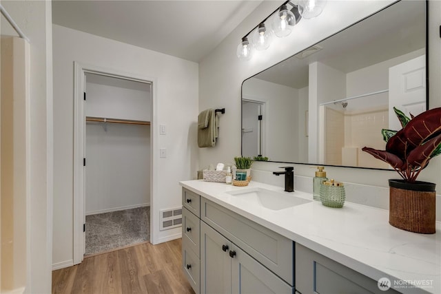 full bathroom with a walk in closet, visible vents, walk in shower, wood finished floors, and vanity